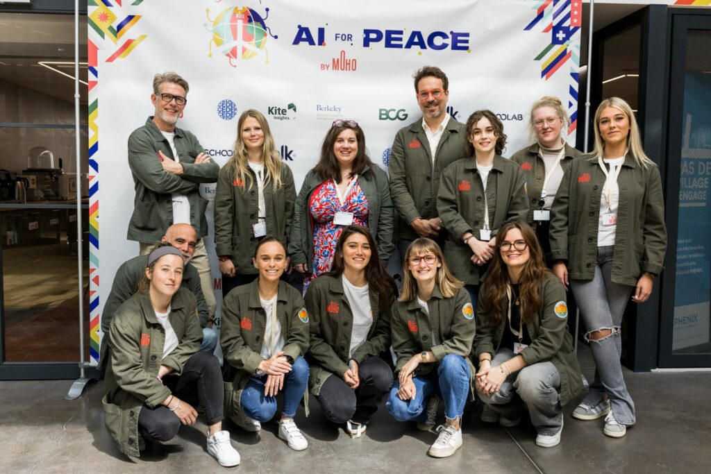 L'image est une photo sur laquelle on peut voir différents membre de l'équipe du MoHo (13 d'entre eux),, posant devant un visuel préparer pour le lancement du nouveau programme AI for Peace